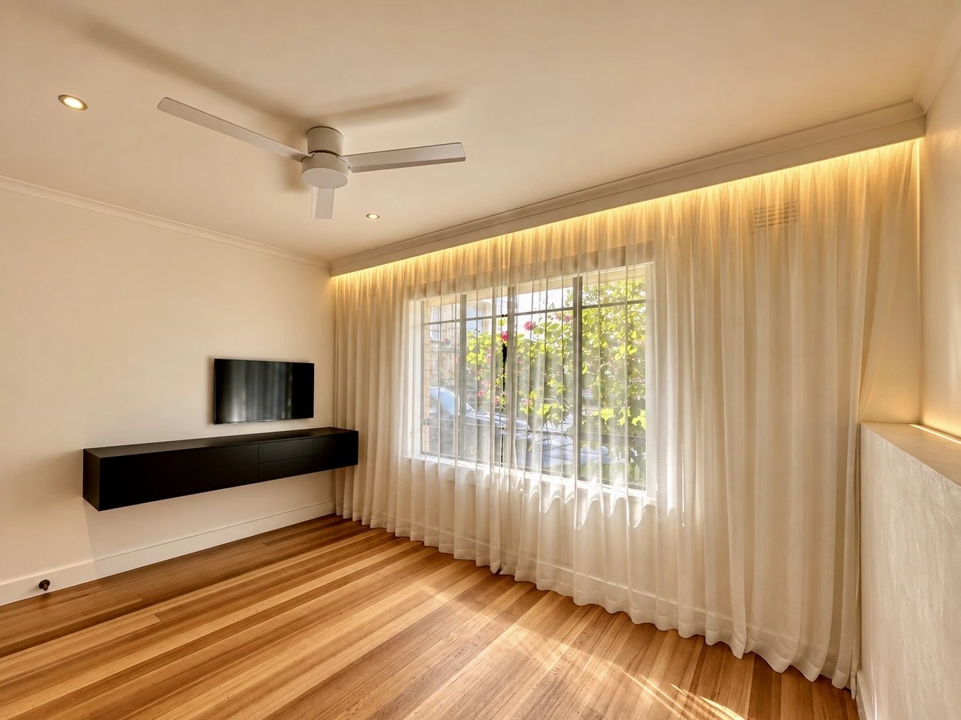 Finished living room with timber floors, sheer curtains and a wall-mounted TV unit